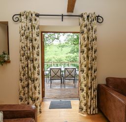 A doorway with floral curtains opening to a wooden deck with a table and chairs at Nant Glas Pumpsaint near Lampeter