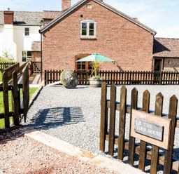 A fenced outdoor area with gravel and a brick house in the background at The Cider House in Leominster