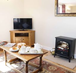 A living room with a wooden coffee table set with tea cups and cake near a television and electric stove at The Cider House in Leominster