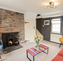 A living room with a stone fireplace and wood stove a colorful coffee table and chairs at Kooky Cottage in Brecon