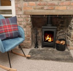 A rocking chair with a plaid pillow next to a wood burning stove in a brick fireplace at Kooky Cottage in Brecon