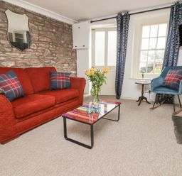A living room with a red sofa and blue rocking chair next to a window and a multicolored coffee table with flowers at Kooky Cottage in Brecon