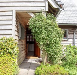 The entrance to a wooden house with plants and bushes around the pathway at Bybrook Lodge in Davidstow near Camelford