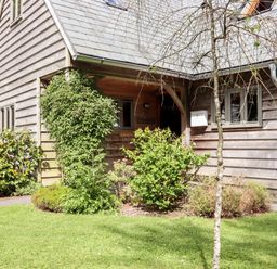An exterior view of a wooden house with a porch surrounded by bushes and grass at Bybrook Lodge Davidstow near Camelford