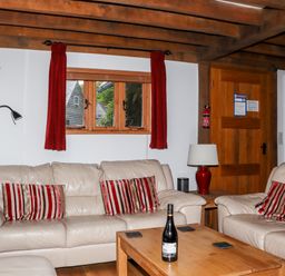 A living room with beige leather sofas red striped cushions wooden beams and a wooden coffee table with a bottle at Bybrook Lodge in Davidstow near Camelford