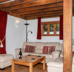 A living room with beige leather sofas red curtains wooden coffee table and a bottle at Bybrook Lodge Davidstow near Camelford