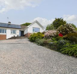 A house with solar panels on the roof and a gravel driveway with plants and bushes at The Dingle in Wisemans Bridge near Stepaside
