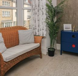 A living room with a wicker sofa and blue drawer unit at Still Waters in Swanage