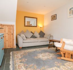 A living room with a sofa, armchair, wooden chest, wall mirror, and a lamp at Hill Coach House in Watchet