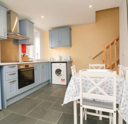 A kitchen with blue cabinets a washing machine and a dining table with chairs at Hill Coach House in Watchet