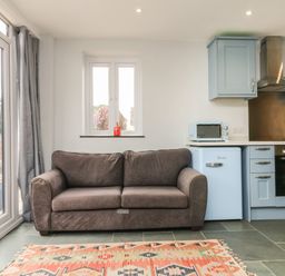 A kitchen area with a gray sofa a patterned rug and blue cabinets at Hill Coach House in Watchet