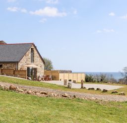 A stone house with a slate roof and outdoor seating area on a grassy slope with a view of the sea at Apple Blossom Barn in Gulval near Penzance