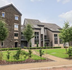 Modern residential buildings with stone and grey walls and multiple windows surrounded by green grass and small trees at Rivers Edge in Newby Bridge