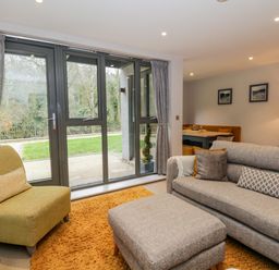 A living room with grey sofa yellow armchair and large windows overlooking a garden at Rivers Edge in Newby Bridge