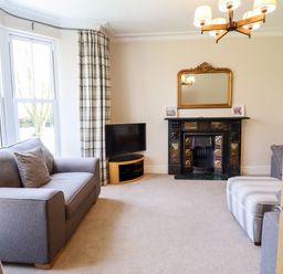 A living room with sofas a striped ottoman a fireplace with a mirror above and a television at Craigside in Betws-Y-Coed