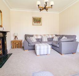 A living room with a grey sectional sofa and striped ottoman near a fireplace at Craigside in Betws-Y-Coed