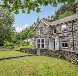 A stone house with a grassy yard and trees around at Craigside in Betws-Y-Coed