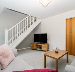 A living room with two sofas a wooden coffee table a television on a wooden stand and stairs at 16 Mythern Meadow Bradford-On-Avon