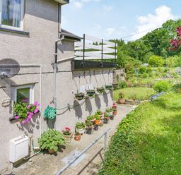 Side of a house with potted plants and hanging flower baskets next to a garden at Kavieng in Glangrwyney near Gilwern
