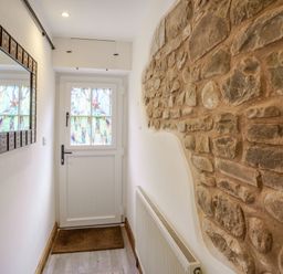 A hallway with a white door with stained glass windows a stone wall a radiator a mirror and a doormat at Kavieng in Glangrwyney near Gilwern