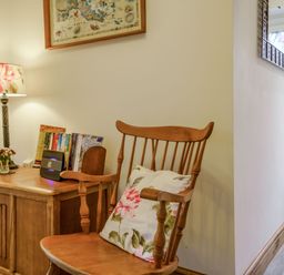 A wooden chair with a floral cushion next to a wooden cabinet with a lamp and books at Kavieng in Glangrwyney near Gilwern