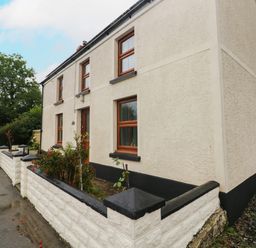 Exterior of a two-story house with white walls and wooden framed windows surrounded by a low white wall at Brynawel in Llangynin near Llanboidy