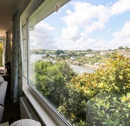 A living room with armchairs and curtains overlooking a river and houses at Rathillet in Feock near Truro