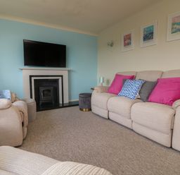 A living room with beige sofas with colorful cushions a fireplace with a mounted TV and framed pictures on the wall at Rathillet in Feock near Truro