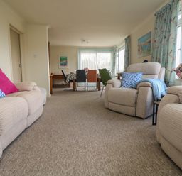 A living room with beige sofas and colorful cushions a dining table with multiple chairs and floral curtains at Rathillet in Feock near Truro