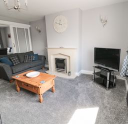 A living room with a grey sofa wooden coffee table fireplace TV and curtains at Fisherman's Row in Amble
