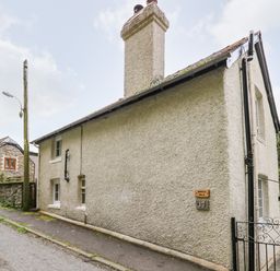 A stone cottage with chimneys next to a narrow road at Myrtle Villa in Knighton