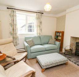 A living room with two cream chairs a blue sofa an ottoman a wood stove and a bookshelf at Myrtle Villa in Knighton