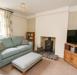 A living room with a sofa ottoman wood stove and television on a cabinet at Myrtle Villa in Knighton