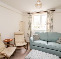 A sitting room with two beige armchairs a blue sofa with patterned cushions and an ottoman near a window at Myrtle Villa in Knighton