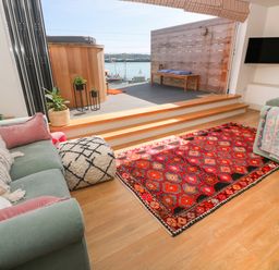 A living room with green sofas and a red patterned rug leading to a deck with a wooden bench and hot tub at 16 Arwenack Street in Falmouth