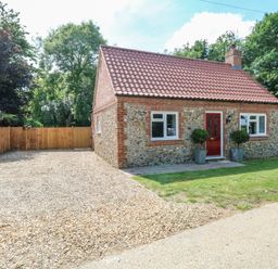 A small brick house with a red door and gravel driveway surrounded by wooden fences and trees at Keepers Cottage Beeston near Dereham