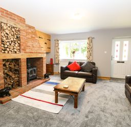 A living room with two brown leather sofas a wooden coffee table a brick fireplace and a window at Keepers Cottage in Beeston near Dereham