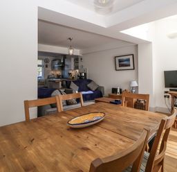 A dining area with a wooden table and chairs adjacent to a living room with sofas a TV and a blue armchair at Ferriwais in Appledore