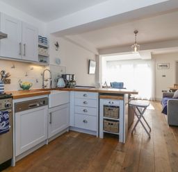 A kitchen with white cabinets and wooden countertops open to a living area with a sofa and dining table at Ferriwais in Appledore