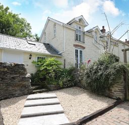 Exterior view of a two story stone house with a gravel path and garden with plants and bushes at Spring Cottage in Pentre Cwrt