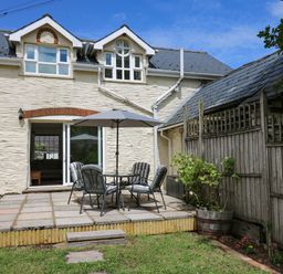 An outdoor patio with a table umbrella and chairs next to a white stone house with windows and a wooden fence at Spring Cottage in Pentre-Cwrt