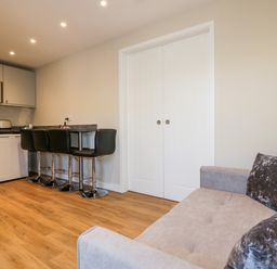 A small kitchen area with appliances and bar stools next to a sofa in a living space at The Granary in Helland near Bodmin