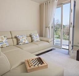 A living room with a beige sectional sofa with patterned cushions a chessboard on the sofa glass side table and a wall-mounted television at Crowthers in Dartmouth