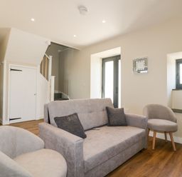 A living room with a gray sofa and two round chairs near a staircase and windows at The Hayloft in Helland near Bodmin