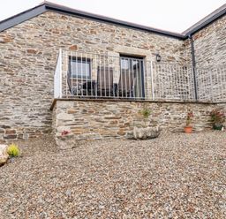 An outdoor stone patio area with a stone wall and a small balcony with chairs and a table at The Hayloft in Helland near Bodmin