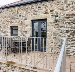 A stone wall balcony with metal railing table and chairs at The Hayloft in Helland near Bodmin