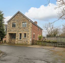 A stone and brick house with a driveway and wooden fence at Ridley Lodge in West Thirston felton