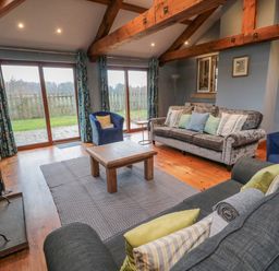 A living room with wooden beams a fireplace two sofas two armchairs a coffee table and large glass doors at Ridley Lodge in West Thirston felton