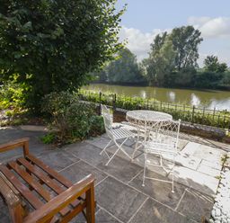 An outdoor patio with a wooden bench and white metal table and chairs by a river at Florence Villas in Worcester