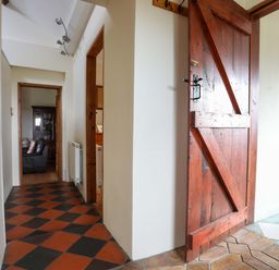 A hallway with red and black checkered floor tiles and a wooden door leading to adjacent rooms at Penrallt Fawr in Rhosgadfan near Waunfawr